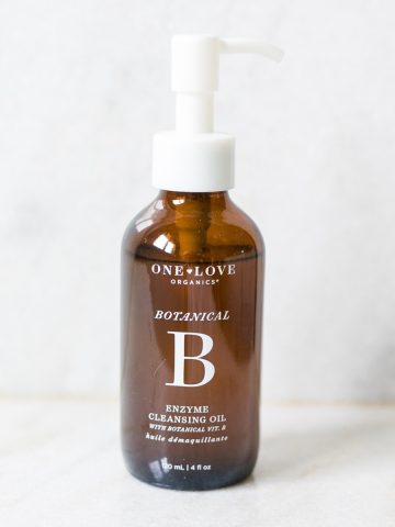 bottle of one love organics botanical b cleansing oil on white marble background.