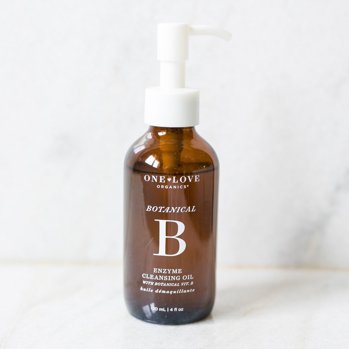 bottle of one love organics botanical b cleansing oil on white marble background.