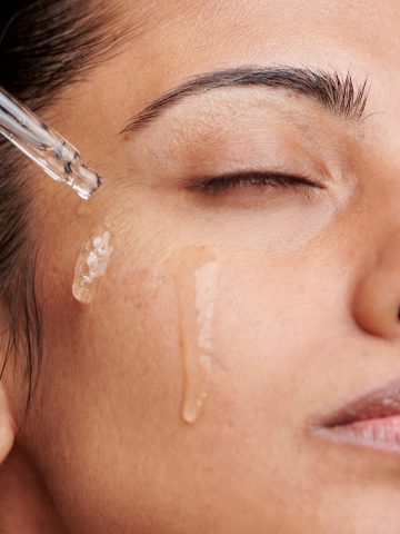 closeup of woman's face with facial serum dripping on her cheek.